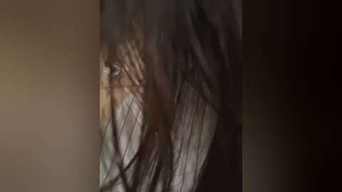 Media: A video captures a close-up of a person's face, partially obscured by long, dark hair. The lighting is dim, creating a moody, almost ethereal atmosphere. The skin tone appears pale, and the overall tone of the image is dark and mysterious.