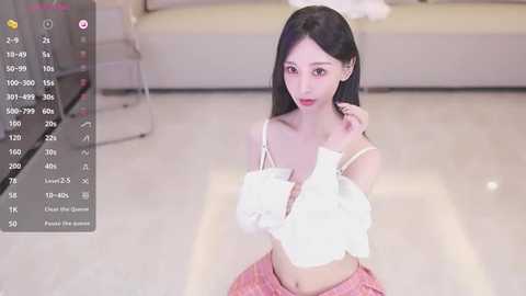 Media: A young East Asian woman with long black hair, fair skin, and a slim figure, wears a white off-shoulder top and pink plaid skirt, kneeling on a polished floor in a modern living room.