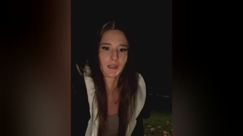 Media: A video of a woman with long brown hair, wearing a white jacket, speaking into a dark night sky.