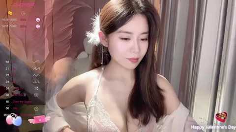 Media: Video of a young Asian woman with long brown hair, wearing a white lace bra, standing indoors. The background features a blurred reflection.