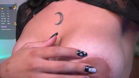 Media: Video of a close-up of a woman's breast with a crescent moon tattoo and black and white nail polish, partially covered by a black lace bra.