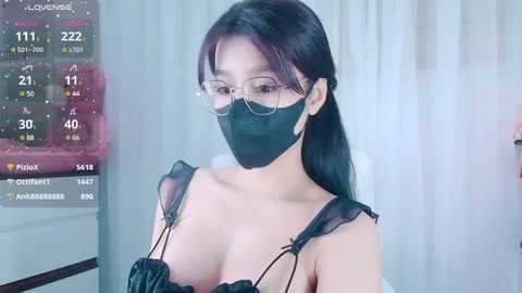 Media: Video of an Asian woman with long black hair, wearing a black face mask, glasses, and a black lace top, in a modern, brightly-lit room with a digital clock displaying 10:23.