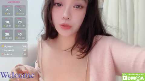 Media: Video of an Asian woman with long black hair, fair skin, and small breasts, wearing a pink sweater, taken indoors. Background shows a chart with \"Live\" and \"Watch\" options.