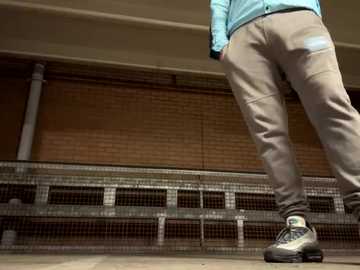 Media: Video of a person in a blue jacket, beige pants, and white sneakers, walking on a metal grate in a dimly lit, brick-walled, industrial room.