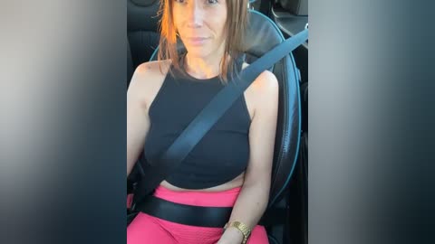 Media: Video of a young woman with shoulder-length brown hair, wearing a black sports bra and high-waisted pink leggings, sitting in a car with a seatbelt on.