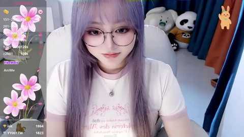 Media: A video of a young Asian woman with long, pastel purple hair, wearing glasses, a white t-shirt, and a necklace, sitting on a white chair in a room with a panda plush toy.