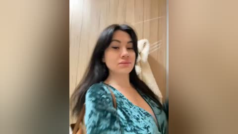 Media: A video of a young woman with long, dark hair, wearing a teal velvet dress, standing in a bathroom with beige tiles and a white towel.