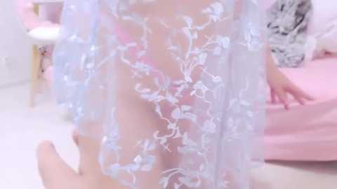 Media: Video of a fair-skinned woman in a sheer, floral-patterned babydoll dress, standing in a pink bedroom with a white floor, blurred background.