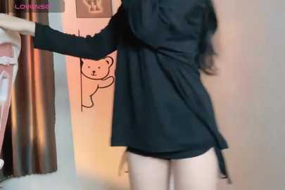 Media: Video of a slender, light-skinned woman in a black robe, leaning against a wall with a teddy bear print.