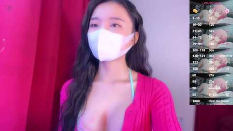 Media: A video of an Asian woman with long black hair, wearing a white surgical mask, pink top, and revealing cleavage, against a red background.