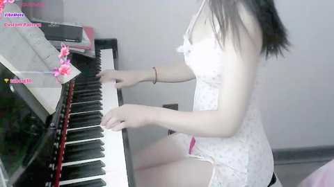 Media: Video of an Asian woman in a white lace dress, playing a piano, with a pink bow in her hair.