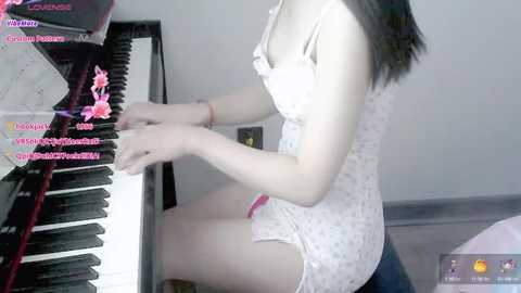 Media: Video of a light-skinned woman with straight black hair playing a black grand piano in a dimly lit room. She wears a white lace dress.