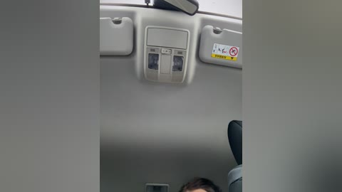 Media: A video of a car's interior ceiling shows a compartment with two USB ports and a yellow warning sign. The ceiling is light gray, and a person's head is partially visible in the bottom right corner.