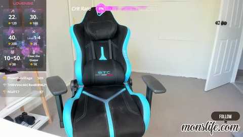 Media: Video of a modern, high-end black gaming chair with blue accents, positioned in a minimalist, well-lit room with a white door and a TV displaying a game interface.