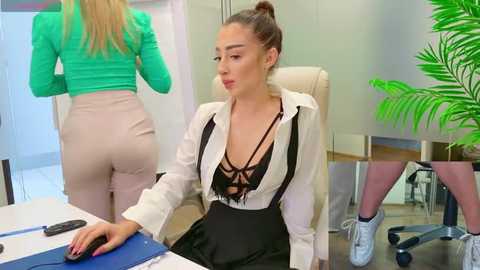 Media: Video of a blonde woman in a green top and beige pants, facing a brunette woman in a white blouse and black skirt, seated at a desk in an office.