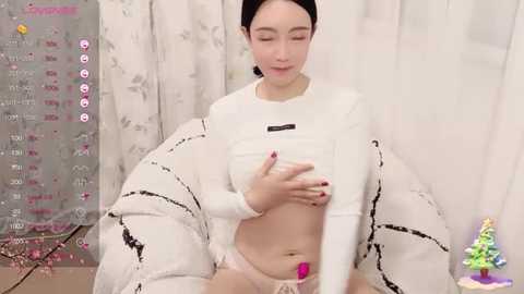 Media: A video of an Asian woman in a white crop top and pink panties, sitting on a white bean bag, with a festive background featuring a calendar and a small Christmas tree.