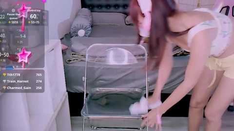 Media: A blurry photo shows an Asian woman in a maid outfit, dusting a clear chair in a modern bedroom with grey bedding and a white nightstand.