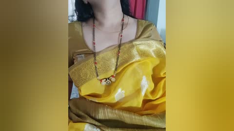 Media: Video of a woman wearing a golden yellow saree with intricate floral designs, draped elegantly, adorned with a red beaded necklace, and a hint of her dark hair.