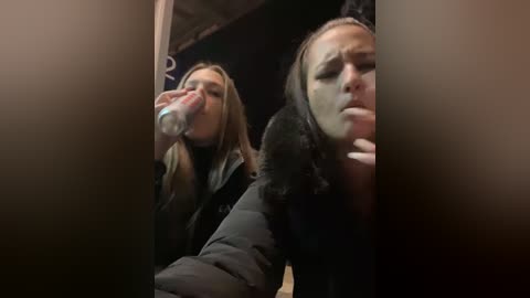 Media: Video of two women drinking from a water bottle in a dimly lit room; one with light brown hair, the other with dark hair.