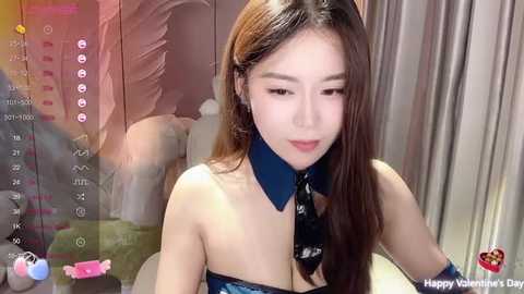 Media: Video of an East Asian woman with long brown hair, wearing a strapless black and blue Valentine's Day-themed outfit, in a modern, dimly lit room.