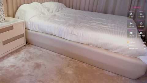 Media: Video of a modern bedroom with a white, upholstered bed against beige walls, a white nightstand with drawers on the left, and a soft, plush carpet. Digital overlay shows a fitness app with heart rate and distance metrics.