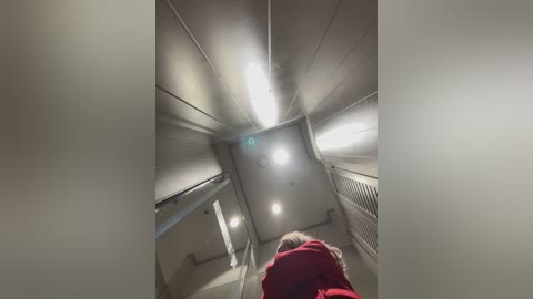 Media: Video of a narrow, dimly lit stairwell with white walls, fluorescent lights, and a red jacket visible at the bottom.