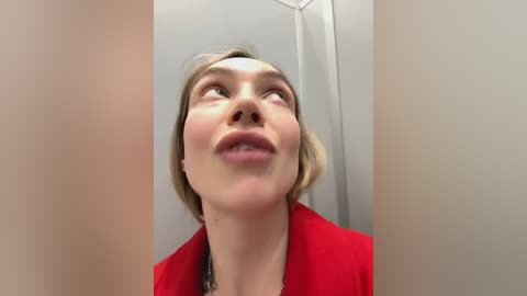 Media: A video of a woman with short, blonde hair, fair skin, and a red jacket, looking up with a slight smile, surrounded by two large, pale vertical objects.