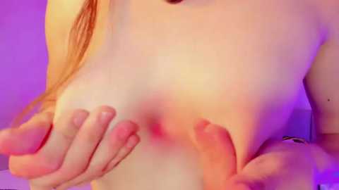 Media: Video of a light-skinned woman with long, straight red hair, topless, pressing her breasts together. Her nipples are slightly erect, and her hands are holding them. The background is a soft, purple-hued gradient, adding a sensual ambiance.