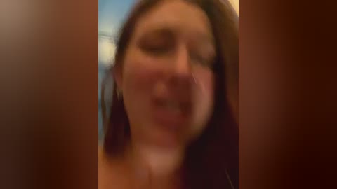 Media: A blurry video of a woman with fair skin and long brown hair, eyes closed, possibly in pain or emotional distress, with a blurred background suggesting an indoor setting.