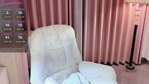 Media: A video of a cozy, modern living room with a plush white armchair, soft pink curtains, and a tall, glass lamp on a beige carpet. A digital overlay shows a weather forecast.