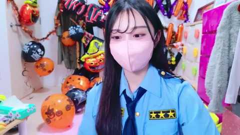 Media: Video of a young Asian woman with long black hair, wearing a blue police uniform, mask, and yellow star badge, surrounded by Halloween decorations in a brightly lit room.