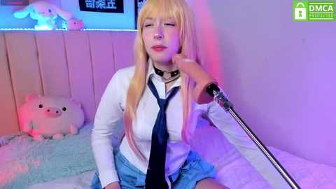 Media: Video of a blonde woman in a white shirt, tie, and blue skirt, singing into a microphone, surrounded by plush toys in a softly lit room.