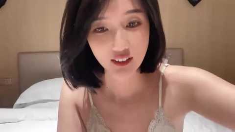 Media: Video of an Asian woman with straight, shoulder-length black hair, wearing a light-colored lace bra, lying on a bed in a bedroom with beige walls.