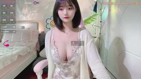 Media: Video of a fair-skinned, slim Asian woman with straight black hair and large breasts, wearing a revealing white lace lingerie set, sitting on a bed in a bedroom with floral decor.