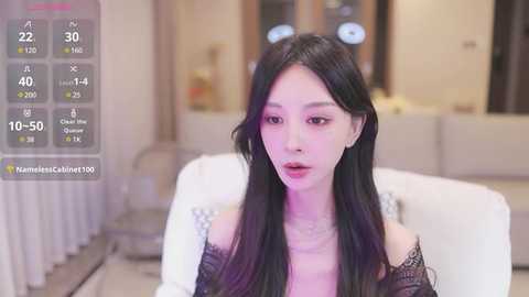 Media: A video of a young East Asian woman with long black hair, pale skin, and light makeup, sitting in a modern living room with a white couch, beige walls, and a clock visible.