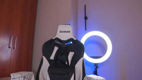 Media: A video of a white and black gaming chair with the \"Razer\" logo, positioned in a dimly lit room with a large round ring light emitting a blue glow.