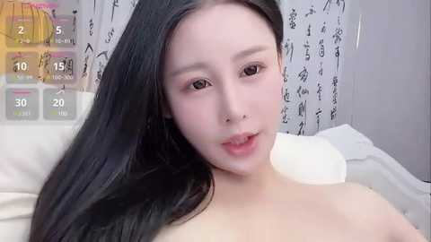 Media: Video of a young East Asian woman with long black hair, fair skin, and light makeup, lying topless on a bed. The background features a white curtain with Japanese characters.