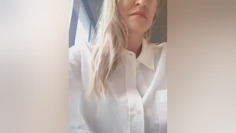 Media: Video of a woman with light skin and blonde hair, wearing a white blouse, partially obscured by two vertical, blurred white panels.