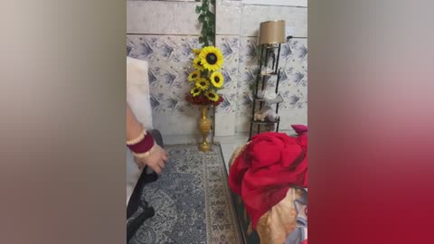 Media: A video of a tiled room with a sunflower arrangement, a bed with red sheets, and a person in a white shirt and red bracelet.