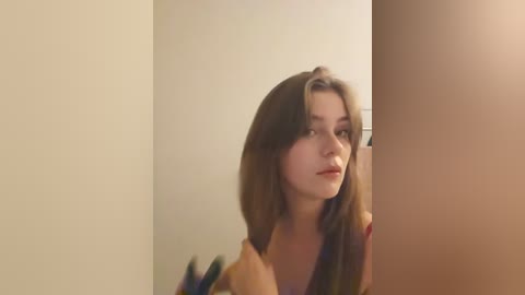 Media: A video of a young woman with light skin and shoulder-length brown hair, wearing a light-colored top, looking towards a mirror, slightly out of focus.