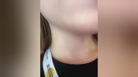 Media: A blurred, close-up video of a person's neck and face, showing pale skin and a black t-shirt with a yellow logo. The background is indistinct.