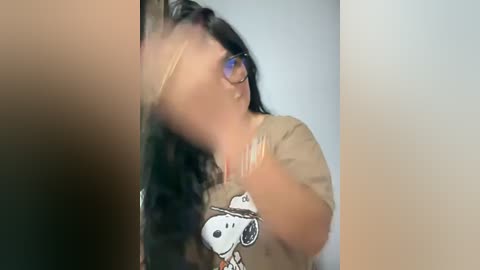 Media: A blurry video shows a woman with long, wavy dark hair, wearing glasses and a beige t-shirt with a cartoon dog.