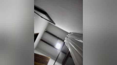 Media: A blurred video of a modern, minimalist room with a ceiling light, white curtains, and a dark wooden door. The image is slightly out of focus, giving a dreamy, hazy effect.