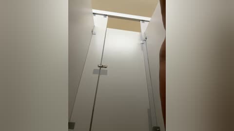 Media: A video of a narrow, white-walled hallway with a glass door and a metal handle in the middle, leading to a dimly lit, rectangular room with beige walls and a wooden door on the right.