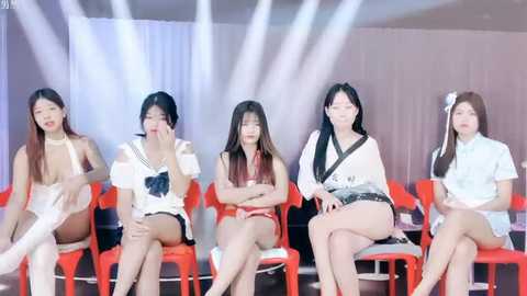 Media: Video of five Asian women, diverse in age and style, seated on red chairs against a white backdrop, wearing casual to semi-formal outfits.