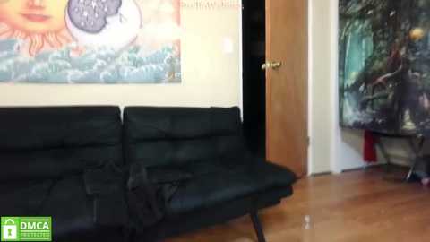 Media: Video of a cozy living room with a black leather sofa, a colorful abstract wall mural, and a wooden door partially open.