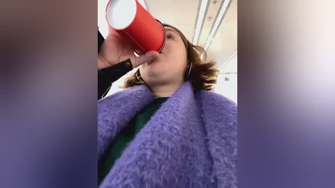 Media: A video captures a woman in a purple fleece jacket, drinking from a red cup, indoors with blurred background.