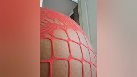 Media: Video of a close-up of a person's lower body, wearing bright red fishnet stockings with large, square holes. The skin tone is light, and the background shows a white door and part of a room with soft lighting.