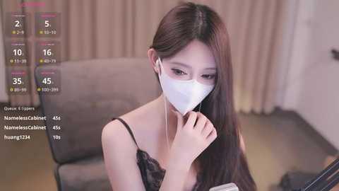 Media: Video of an East Asian woman with long brown hair, wearing a white mask and black lace top, seated indoors, with a digital health tracker interface overlaid.