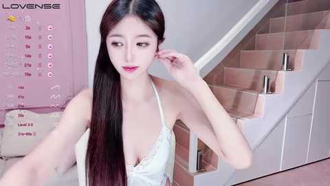 Media: A video of a slender, pale-skinned Asian woman with long, straight black hair, wearing a white lace bralette, posing on a staircase with a pink wall calendar in the background.